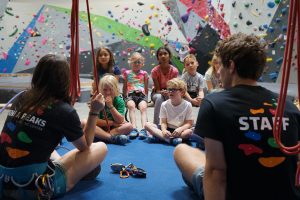 Kids sitting around in circle in the middle of an indoor rock climbing gym